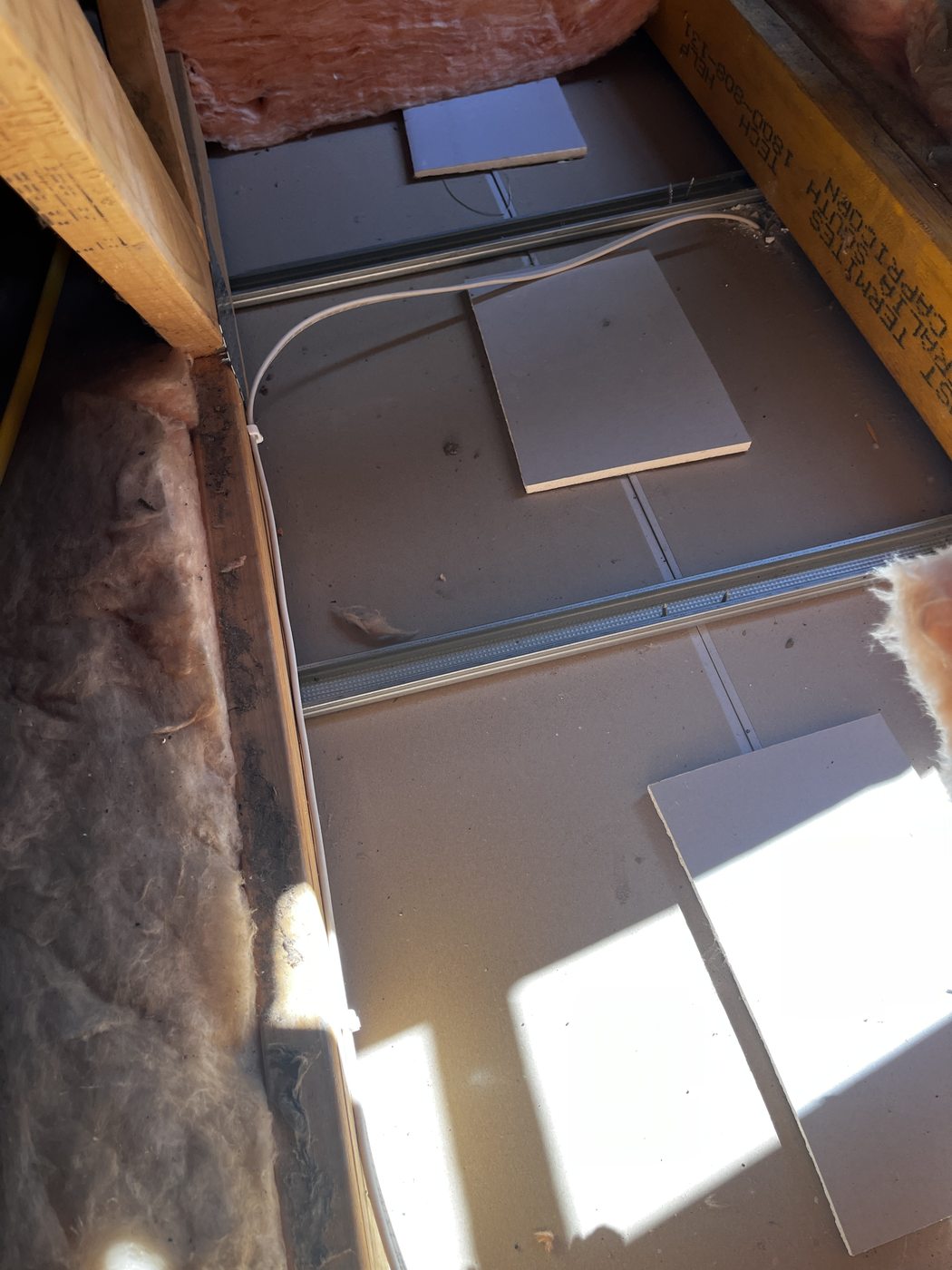 Roof space above a plasterboard ceiling showing the new fan cable clipped clear of the plaster and the insulation pulled back, by SALTD Electrical