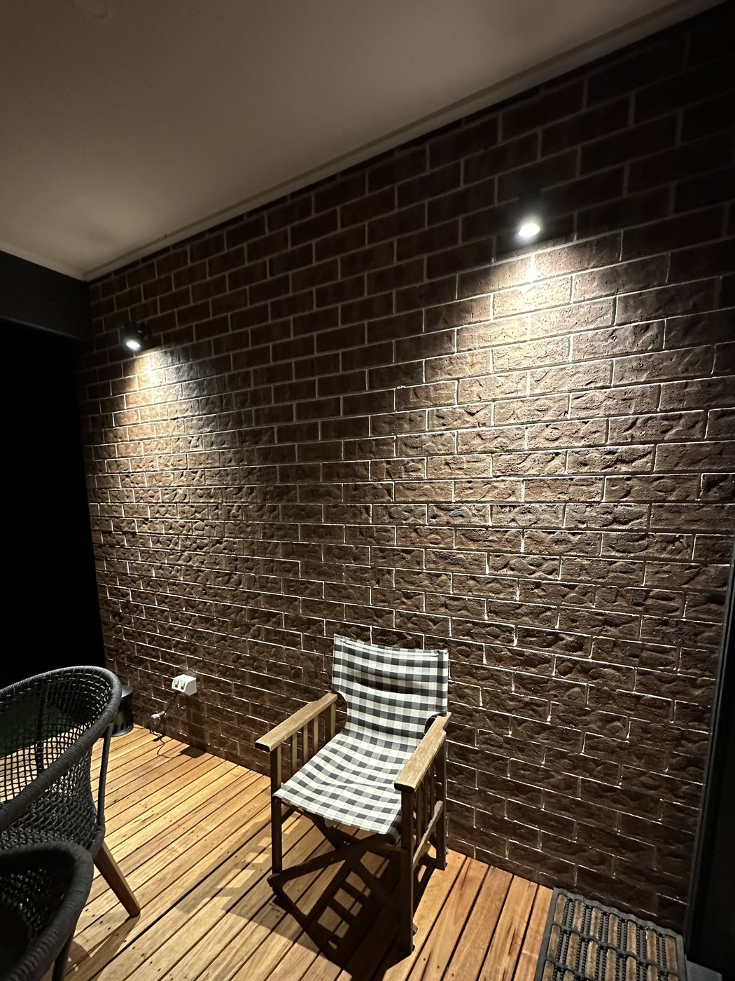 Alfresco deck at night with two downlights washing scallops of light down a dark brick feature wall, installed by SALTD Electrical