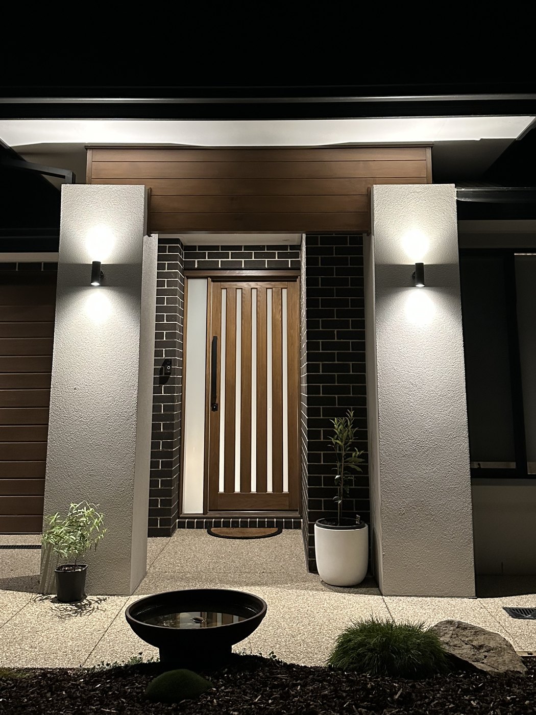 Front entry at night with two up-and-down wall lights either side of a timber slat door and a lit soffit above, installed by SALTD Electrical