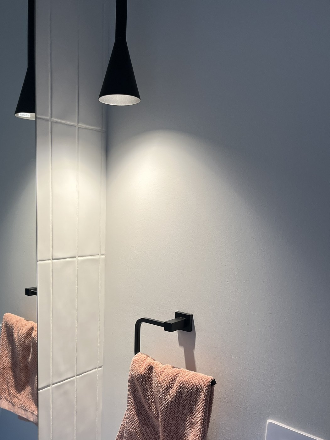Black cone pendant light hung beside a mirror in a powder room, throwing light down the wall, installed by SALTD Electrical
