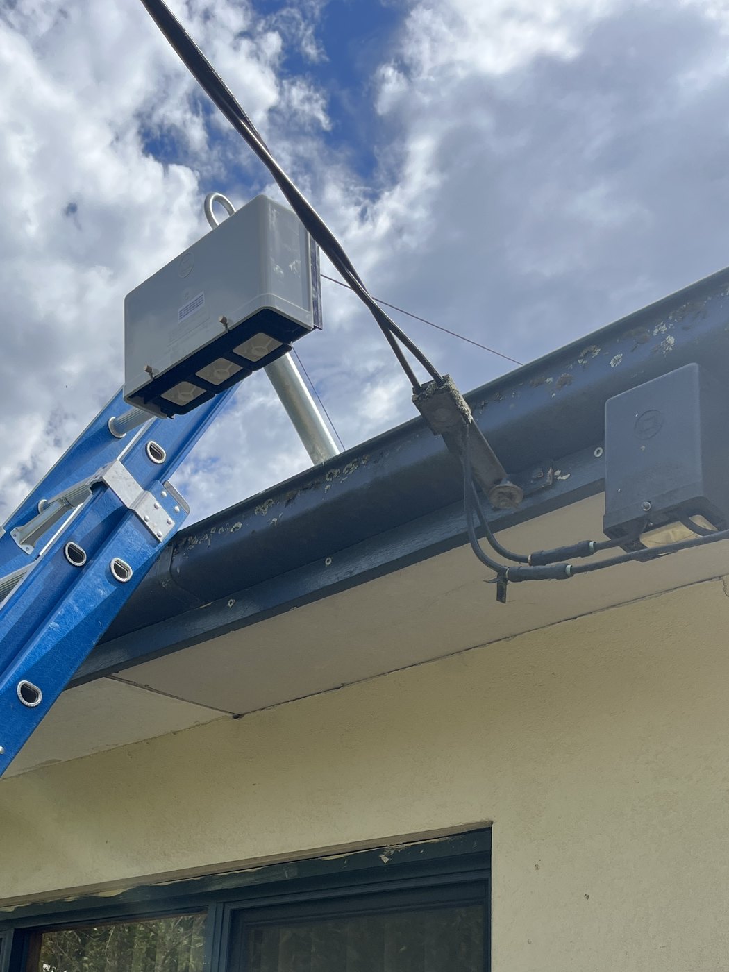 New three-phase point of attachment enclosure on a galvanised mast, with the superseded single-phase connection box still on the fascia beside it